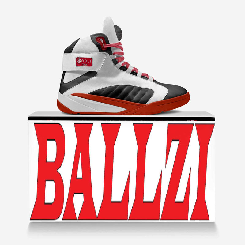 A high-top basketball sneaker in white, black, and red, displayed on top of a white block with large red 'BALLZI' lettering on the front, against a light gray background.